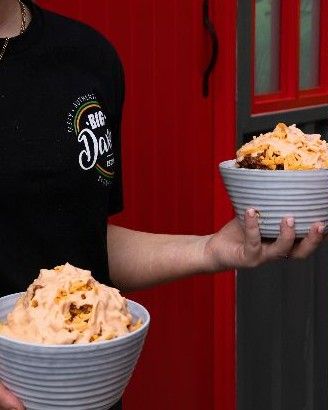 A server in a Big Dave's t-shirt holding two bowls of loaded chips by a red door