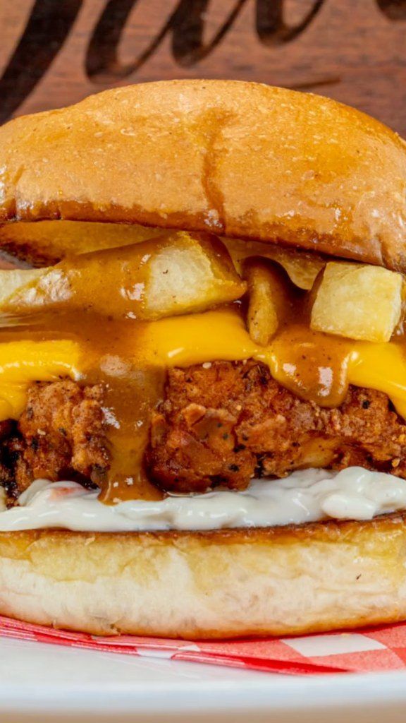 A crispy chicken burger stacked with chips, melted cheese and curry sauce