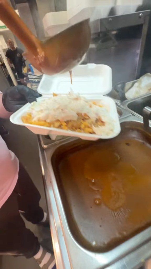 Curry sauce being ladled over a box of chips